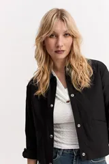Chaqueta liviana color beige, de corte recto, con cuello camisero, cierre frontal con broches y bolsillos aplicados.