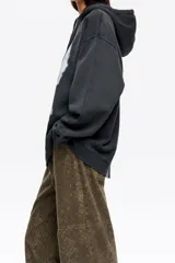 Hoodie de algodón color negro con efecto lavado, corte oversize y capucha con cordones ajustables. Presenta un estampado gráfico frontal con paisaje, lobos y rayos, junto con el logo de la marca.