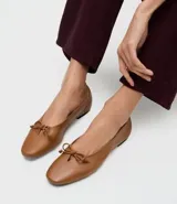 Zapatilla tipo bailarina Satinato confeccionada en cuero color tostado, con punta redondeada y detalle de mini lazo en la parte superior. Cuenta con suela plana de baja altura.