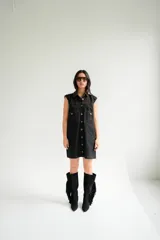 Vestido corto de jean color gris oscuro con efecto acid wash, sin mangas, con cuello camisero y cierre frontal de botones. Incluye dos bolsillos en el pecho con solapa y pespuntes decorativos.