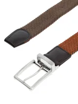 Cinturón elástico de tejido trenzado con terminaciones en cuero y hebilla metálica reversible en color plata vieja.