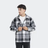 Camisa de franela a cuadros en tonos grises, blancos y negros, forrada con corderito sintético en el interior. Cuenta con mangas largas, bolsillos con solapa en el pecho y cierre frontal con botones.