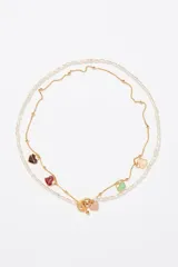 Collar de doble cadena, una de perlas irregulares y otra de eslabones dorados con pequeñas bolitas. La cadena dorada tiene dijes colgantes en forma de corazón esmaltados en varios colores (marrón, vino, verde menta, rosa pálido). El cierre es tipo toggle dorado.