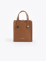 Cartera tipo tote de Jazmin Chebar, color tostado, con diseño estructurado y detalles metálicos en forma de llama en la unión de las asas.