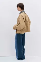 Cazadora de corte oversize en color beige, con cuello de solapa en contraste de color oscuro, cierre frontal con botones y bolsillos laterales.