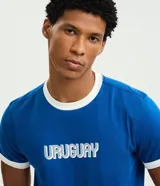 Remera de algodón color azul con cuello redondo y bordes de mangas en color blanco. Presenta la palabra 'URUGUAY' bordada en el centro del pecho con letras blancas y contorno azul.