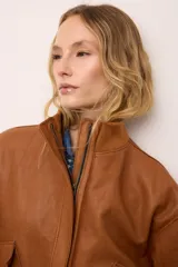 Chaqueta de cuero estilo bomber, con cuello alto, puños y cintura de tejido de punto acanalado. Presenta cierre frontal con cremallera y dos bolsillos laterales con solapa.