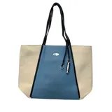Cartera tipo tote de diseño tricolor en tonos beige y azul, con correas largas negras y detalle de dije metálico colgante.