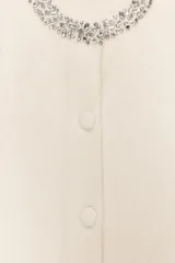 Chaqueta de punto de lana con manga corta, cuello redondo decorado con abalorios joya y cierre frontal con botones forrados a tono.
