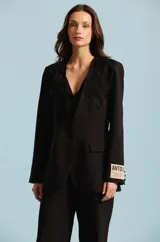 Saco sastre de mujer color negro, con apliques bordados de pedrería en los hombros, solapas cruzadas, cierre frontal de un botón y bolsillos con solapa.
