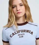 Remera celeste de corte ajustado, con mangas cortas, cuello redondo y ribetes en color marrón oscuro. Presenta la inscripción "California Artists Club" en el pecho en tono marrón.