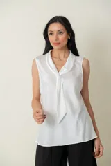 Blusa blanca sin mangas con cuello drapeado que termina en lazo.