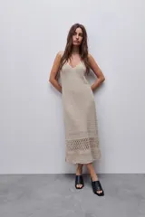 Vestido midi de tejido crochet color beige, con silueta recta y calce relajado. Diseño sin mangas, escote en V y detalles calados en la parte inferior, con terminación ondulada en el ruedo.