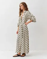 Vestido camisero largo de viscosa y seda, color blanco con estampado de lunares negros. Presenta cuello camisero, mangas largas abullonadas y un cinturón ajustable del mismo género.