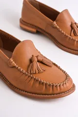Mocasines negros de cuero con borlas y costuras decorativas.