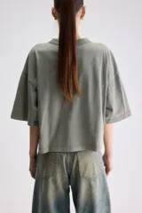 Remera cropped blanca de calce relajado, con cuello redondo, hombros caídos y mangas cortas. Presenta un pequeño detalle de etiqueta bordada en el lateral inferior.
