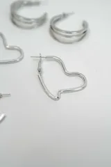 Set de tres pares de aros plateados de diferentes diseños: un par de aros tipo argolla doble, un par de aros con forma de corazón y un par de aros tipo argolla con textura estriada.