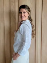 Blusa blanca de manga larga con cuello alto y volados en cuello y hombros.