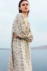 Vestido túnica largo de mezcla de viscosa, con diseño estampado floral en tonos azules y amarillos. Presenta escote en V con frunces, mangas globo con puños elásticos y un cordón fino ajustable en la cintura.