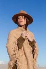 Poncho beige de tejido de punto con flecos y cuello alto.