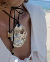 Collar artesanal con dije central de metal con textura orgánica irregular que evoca una ostra. El dije está montado sobre un cordón de algodón natural, permitiendo un uso versátil y regulable.