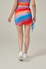 Minifalda con estampado degradado en tonos azul, lila, naranja y rojo. Presenta frunces laterales con cordones ajustables.