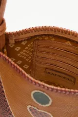 Cartera bandolera de cuero vacuno con diseño patchwork que combina texturas lisas y efecto reptil. Presenta detalles decorativos en forma de círculos y un corazón central, con costuras visibles en los bordes y una borla colgante en el lateral. Incluye correa larga ajustable.
