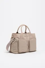 Bolso de mano de Bimba y Lola confeccionado en nylon color beige, con estructura blanda, doble asa superior y correa ajustable extraíble. Presenta dos bolsillos frontales con cierre, logo metálico frontal y cierre principal de cremallera.