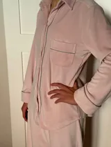 Pijama de dos piezas color rosa pálido, confeccionado en terciopelo. La camisa es de manga larga con botones frontales y bolsillo en el pecho. El pantalón es de corte recto con cintura elástica.