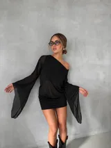 Vestido corto negro de diseño asimétrico con un hombro al descubierto. Presenta mangas largas acampanadas de tela semitransparente y una falda ajustada al cuerpo.