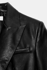 Blazer entallada de cuello solapa y manga larga con hombreras, confeccionada en efecto piel color negro. Cuenta con bolsillos delanteros con solapa y cierre frontal cruzado con botones.