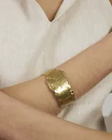 Brazalete rígido de diseño orgánico con textura irregular y acabado artesanal. Pieza abierta ajustable, disponible en bronce o alpaca maciza.