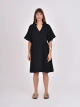 Vestido midi de color negro con cuello en V y mangas cortas tipo kimono. Presenta un corte holgado con cintura ligeramente marcada y falda con vuelo.