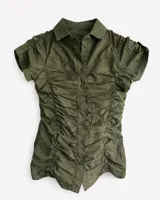 Camisa de manga corta color verde militar, con cuello clásico y cierre frontal de botones. Presenta un diseño entallado con frunces verticales a lo largo de todo el frente y en las mangas.