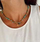 Collar de estilo boho con cuentas de piedra en tonos turquesa y verde, intercaladas con piezas metálicas doradas. Presenta dijes colgantes en forma de luna, estrella y una piedra rectangular.