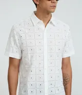Camisa de manga corta para hombre, confeccionada en algodón color blanco con diseño de bordado de flores y perforaciones geométricas. Presenta cuello inglés y cierre frontal con botones.