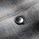 Campera a cuadros gris y negra con cuello de pana negro, cierre con botones, bolsillos de parche en el pecho y corte recto.