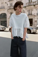 Camiseta blanca de manga corta abullonada y cuello redondo, con detalles de bordados perforados y bajo con doble volante.