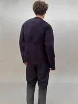 Buzo de lana merino afieltrada color negro con estampado abstracto plateado en el frente. Tiene cuello redondo y puños con forma que cubre levemente la mano. Es más largo en la parte inferior trasera.