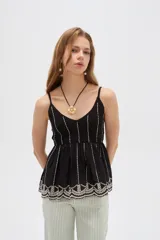Blusa de algodón negra con tirantes finos regulables, escote en V y diseño holgado. Presenta detalles de bordado en color blanco verticalmente en el pecho y un delicado diseño floral bordado en el ruedo.