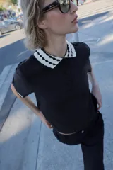 Top de tejido negro con cuello polo y bordes de manga cortos con diseño de ondas en blanco y negro. Tiene un cierre frontal de botones.