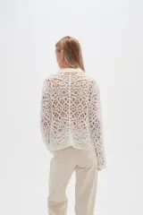 Camisa blanca de crochet con cuello camisero, cierre frontal con botones y dos bolsillos de parche en el pecho.