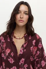Blusa bordó con estampado floral en tonos rosados, confeccionada en algodón Swiss Dot, con mangas largas abullonadas y escote en V con botones frontales.