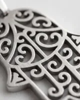 Dije de acero antialérgico con forma de mano de Hamsa, símbolo de protección y buena suerte, con detalles calados.