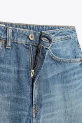 Jeans de tiro medio con diseño baggy barrel, cinco bolsillos y costuras laterales torcidas. Presenta cierre frontal con cremallera y botón metálico.