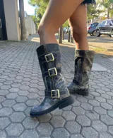 Botas de cuero negro con efecto desgastado, caña alta, cierre lateral y tres correas con hebillas doradas.