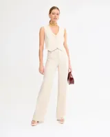 Pantalón de vestir color beige, de corte recto y talle alto, con pinzas frontales y cierre con cremallera, botón y gancho metálico.