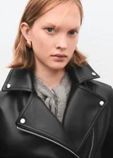 Chaqueta estilo biker de cuero sintético negro, con cierre frontal cruzado, solapas con muesca y broches metálicos.