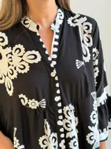 Vestido largo negro con estampado floral blanco, escote en V con cuello mao, cierre frontal de botones y mangas tres cuartos acampanadas.