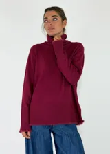 Sweater de cuello alto en color beige, con diseño de punto liso y terminaciones acanaladas en puños y ruedo. Presenta aberturas laterales en el bajo y un detalle de borde desflecado en el ruedo y los puños.